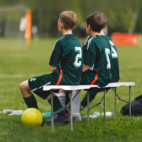 Two kids in soccer uniforms sitting on Six Foot Plastic Folding Bench Set With Handles, Portable HDPE Waterproof Outdoor Seating.