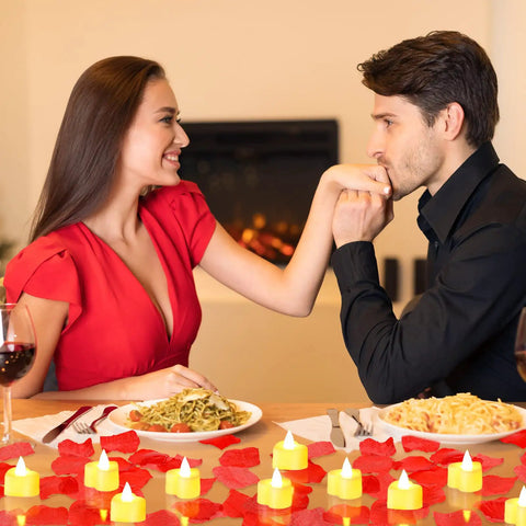 A romantic dinner setting with 6000 Artificial Rose Petals And 72 Heart Shaped LED Tealights For Romantic Nights Valentines Weddings Proposals And Anniversary Decor With Warm White Light scattered on table.