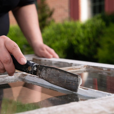Person applying Latex Window Glazing Sealant White 10.1 Oz For Wood And Metal Window Frames Holds Glass In Place