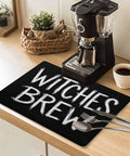 Spooktacular Black Witches Brew Coffee Station Mat Featuring Quick Dry Absorbent PU Material Designed For Kitchen Counter Espresso Machine Setup 28 By 18 Inch Halloween Spill Proof Drip Catch Pad on kitchen counter with espresso machine.