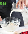 Person pouring liquid from a 50ml Beaker Shot Glasses Set, Heavy Duty Borosilicate 3.3 Glass, 5 Pack With Spouted Beakers into a bowl