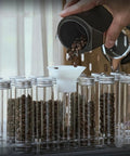 Hype Building Daily Grind Storage Kit With Airtight Single Dose Espresso Canisters, filling glass tubes with coffee beans using funnel.