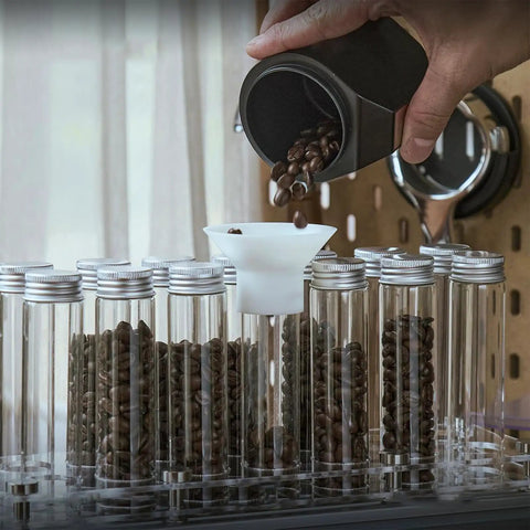 Hype Building Daily Grind Storage Kit With Airtight Single Dose Espresso Canisters, filling glass tubes with coffee beans using funnel.