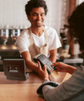 Cashier smiling with a payment terminal in hand, Sturdy Locking Cash Box With Pull Out Tray And Five Compartment Organizer on counter.