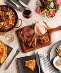 Assorted dishes including paella, sliced meats on a wooden board, fries with dip, and a vegetable salad served on a dining table.