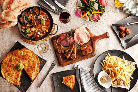Assorted dishes including paella, sliced meats on a wooden board, fries with dip, and a vegetable salad served on a dining table.