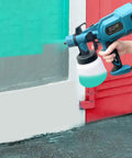 Person using Powerful 800W HVLP Paint Sprayer Kit With Three Copper Nozzle Kits to paint a wall red and green outdoors.