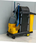 Cleaning cart with mop, broom, yellow caution sign, and bucket on swivel caster wheels in a modern space.