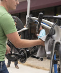 Man wiping a road bike on a repair stand with Waterless Ceramic Bike Cleaner Spray With Pina Colada Scent, 16 Oz, Quick Post Ride Shine, Safe On All Finishes, No Water Needed, Easy Touchup For Road, Mountain, And Gravel Bikes.
