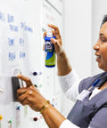 Woman using Killer Dry Erase Whiteboard Cleaning Spray on a whiteboard to remove stubborn ink and ghost marks.