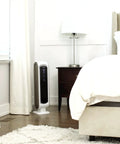 AeraMax 100 Air Purifier With True HEPA Filter And Four Stage Purification next to a bed in a small white bedroom