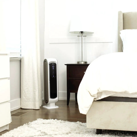 AeraMax 100 Air Purifier With True HEPA Filter And Four Stage Purification next to a bed in a small white bedroom