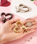 Gold-tone heart-shaped purse turn-lock hardware held in hand; includes 3 sets in gold, silver, and black.