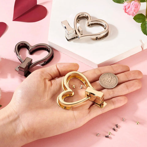 Gold-tone heart-shaped purse turn-lock hardware held in hand; includes 3 sets in gold, silver, and black.