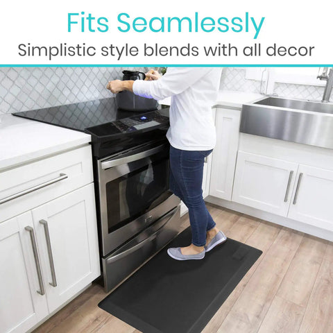 Person standing on black Anti Fatigue Standing Mat For Desk And Kitchen in front of stove, 24 by 36 inches, ergonomic cushioned pad.