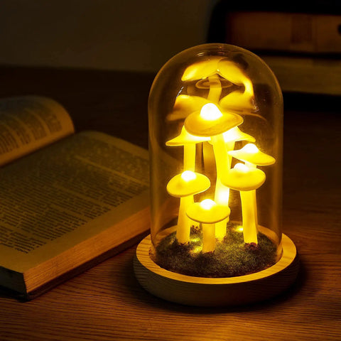Mushroom Night Light In Glass Dome LED Decor With Wooden Base for cozy night ambiance on a wooden table next to open book.