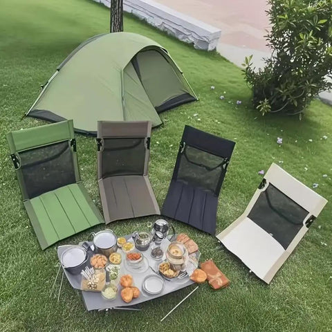 Four foldable mesh-back camping chairs on grass with a picnic spread, near a green tent in a garden setting.