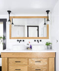 Modern bathroom with wooden vanity, dual sinks, black faucets, and wall lights, featuring a large rectangular mirror.