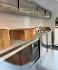 Interior of custom mobile coffee and pastry trailer showcasing a sink, fridge, and stainless steel counters for street vending.