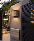 Gold And Black LED Outdoor Wall Light Fixture illuminating a porch area, mounted on a wall near a modern black gate.