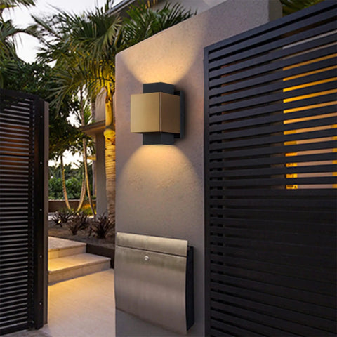 Gold And Black LED Outdoor Wall Light Fixture illuminating a porch area, mounted on a wall near a modern black gate.