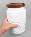 Hand holding a Top Shelf Matte White Glass Storage Jar With Lids Two Pack For Kitchen Organization Airtight Canister.