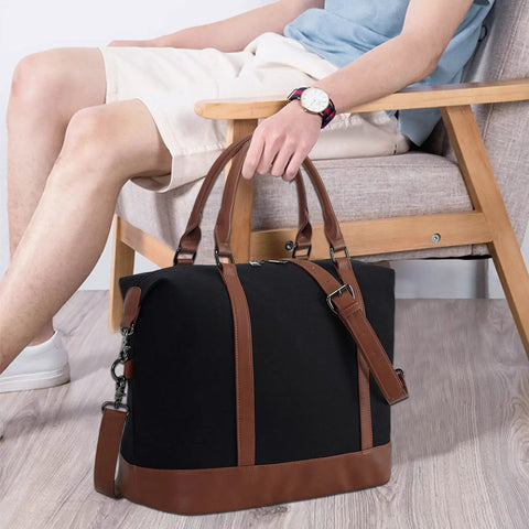 Man seated holding Canvas Travel Tote Bag For Women With Zipper, Weekender Duffel And Carry On Tote, black with brown straps
