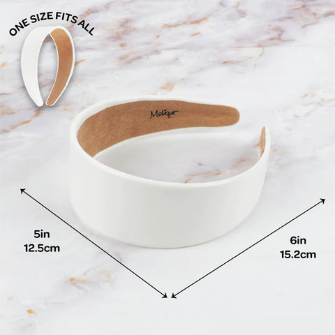 Slay Your Daily Hair Game With This Super Comfy Two Inch White Vegan Leather Headband For Women Featuring Nonslip Inner Lining To Stay Secure During Gym Workouts Or Lazy Sundays And Weekends shown on marble background with dimensions 5in wide and 6in long.