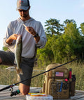 Angler on dock with fish beside All In One Fishing Backpack Tackle Bag With Two Rod Holders Ready To Roll in khaki