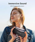 Woman holding Beefy Bass Portable Bluetooth Speaker With Crisp Stereo Sound, IPX7 Waterproof, enjoying music outdoors.