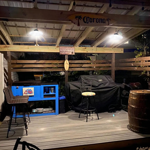 Lit 3000 Lumen Solar Shed Light Hanging Pendant illuminating outdoor gazebo with stools and covered grill at night