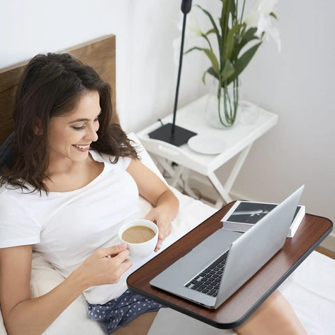 Woman enjoying coffee while using Smooth Rollin Mobile Adjustable Height Portable Computer Desk With Lockable Casters For Top Tier Home Office Standing Laptop Workstation Dark Wood Finish in bed.
