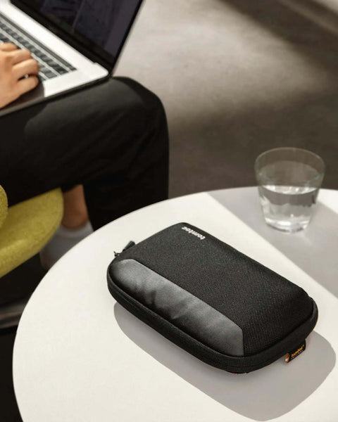 Slick Travel Cable Organizer Pouch With Double Compartments For Portable Charging Cords And Tech Accessories Waterproof Carry Case For Weekend Getaways on a table.