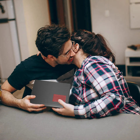 Couple exchanging gift, smiling at table in cozy room setting.