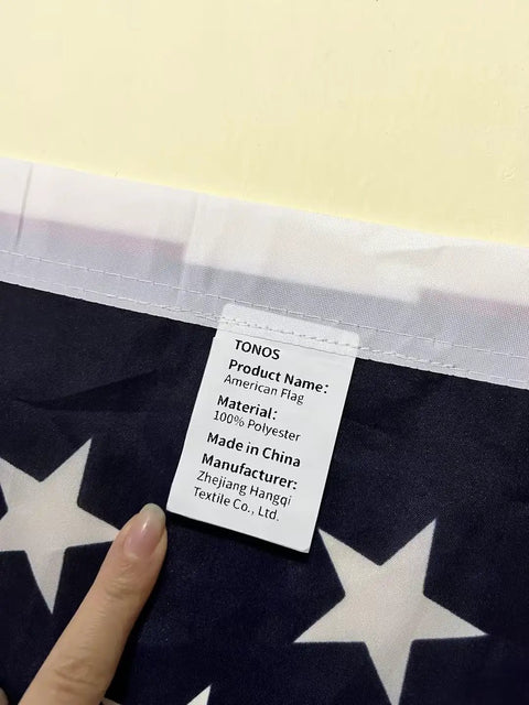 Close-up of the All American Patriotic 3x5 Ft Outdoor Flag With Brass Grommets label showing polyester material and manufacturer info.