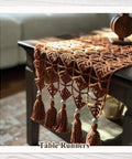 Crochet table runner with tassels on a wooden coffee table.