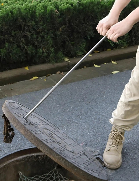Heavy Duty Stainless Steel Manhole Cover Hook With Chunky Thick Handle Rock Solid T Shaped Grip For Pro Contractors And Builders Designed To Haul Heavy Loads Without Breaking A Sweat, lifting a manhole cover.