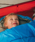 Child smiling in a blue sleeping bag, warm weather sleeping bag for adults and kids, lightweight backpacking gear.