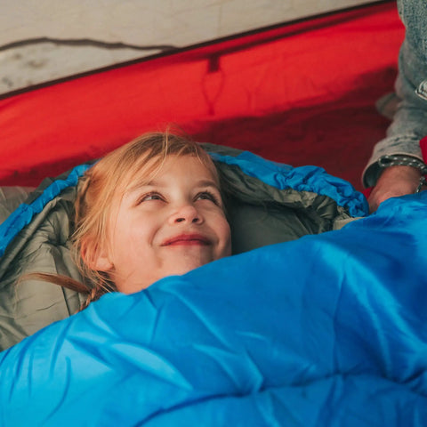 Child smiling in a blue sleeping bag, warm weather sleeping bag for adults and kids, lightweight backpacking gear.