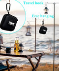 Outdoor scene with lanterns hanging from hooks and a black pouch with travel hook, near a lakeside picnic setup.