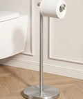 Sturdy Floor Standing Toilet Paper Holder Built Like A Tank In SUS 304 Stainless Steel Rustproof With A 2x Heavier Base And Brushed Nickel Finish For Zero Wobble In Any Bathroom standing in a bathroom with wooden floor and white wall background