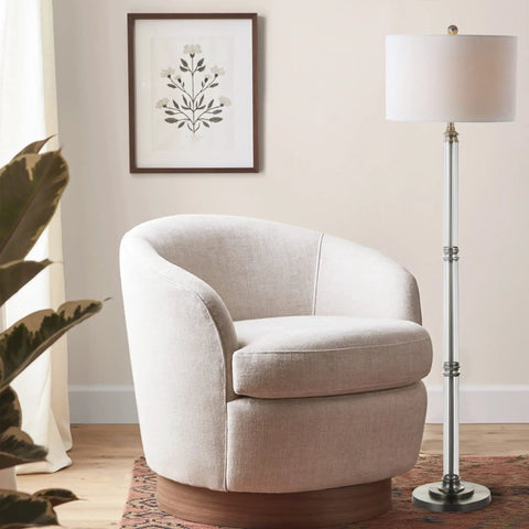 60 Inch Polished Nickel And Clear Glass Floor Lamp With White Linen Round Shade next to living room chair and artwork