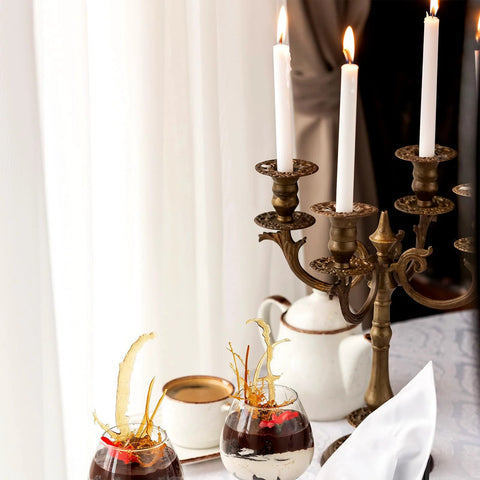Front view of antique brass candelabra with multiple arms and white candles on a dining table