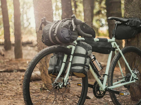 Bike with VersaCage Adventure Cage with Adjustable Mounting System and VersaMount Clamps and Straps for Dry Bags on forest trail
