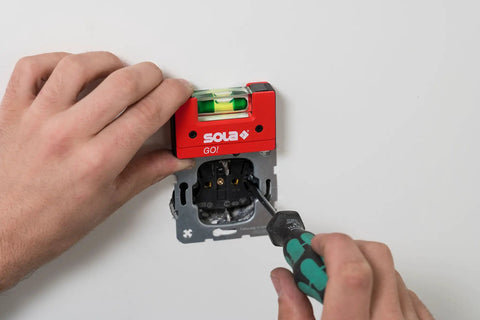 Sola Spirit Level Compact Go! Clip, 0 being used to level an electrical socket with a screwdriver in hand.