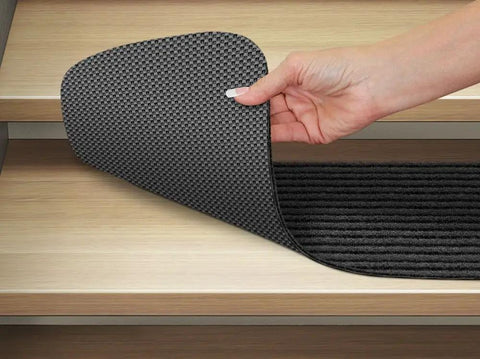 Person placing Set of 15 Skid Resistant Double Ribbed Carpet Stair Treads Smokey Black 9x36 Inches Non Slip Backing on wooden stairs.