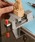 Heavy Duty Cast Iron Bench Vise With 360 Swivel Base Rock Solid Grip For Compact Desk Workholding, holding wooden figure for carving.