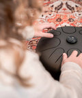 Person playing Super Responsive 16 Inch Steel Tongue Drum With Eight Soothing Notes Comes With Pro Grip Mallets And Carry Bag on a patterned rug.
