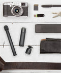 Overhead view of various items including a camera, USB drive, wallet, and parts of Metal Portable Monitor Stand Tripod With 360 Degree Ball Head Phone And Tablet Clamp Desk Mount For Home Office All In One Solution Compatible With Monitors Projectors Cameras Webcams And More on a white wooden surface.