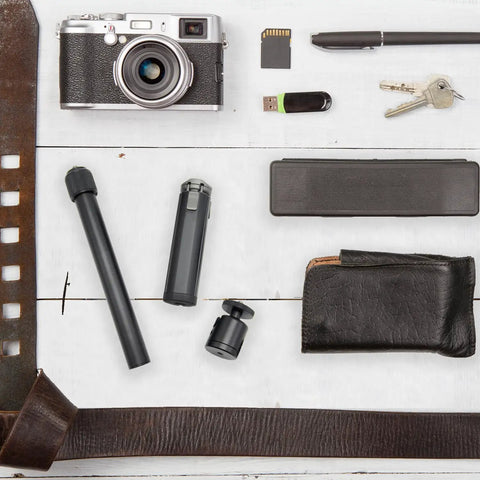 Overhead view of various items including a camera, USB drive, wallet, and parts of Metal Portable Monitor Stand Tripod With 360 Degree Ball Head Phone And Tablet Clamp Desk Mount For Home Office All In One Solution Compatible With Monitors Projectors Cameras Webcams And More on a white wooden surface.